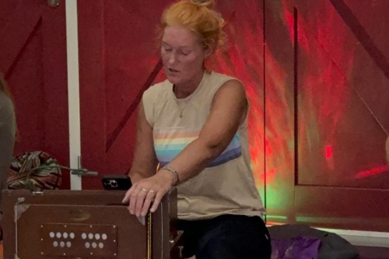 Een man speelt gitaar terwijl een vrouw zingt, beide in een groene omgeving.
