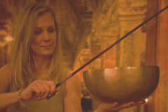 Vrouw die een klankschaal aanraakt in een warme, gloeiende omgeving.