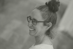 Vrouw met een lach en een knot, draagt een bril, in zwart-wit achtergrond.